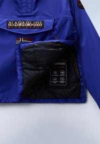 Blue waterproof jacket with a front pocket, black interior lining, branding label, and care instructions on a black tag. Features a Norwegian flag.