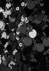 Des sequins circulaires noirs et blancs couvrent une surface texturée, variant en taille et réfléchissant la lumière, certains sequins comportant un trou pour la couture.