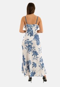 Robe maxi florale blanche avec imprimé de fleurs bleues, dotée de fines bretelles et d'un design fluide, en tissu doux, avec un ourlet légèrement évasé.