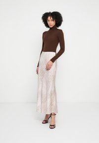 Rjav ohlajen pulover z visokim ovratnikom, združen s tekočo, svetlo roza krilo z nežnim živalskim potiskom. Črni sandali z naramnicami dopolnjujejo videz.