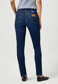 Mörkblå denimjeans med slim fit, försedd med en läderlapp, två bakfickor med zickzackstygn och en klassisk femfickdesign.