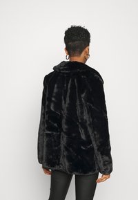 Manteau en fausse fourrure noire avec un large col, présentant une texture douce et une coupe ample. Vue de dos affichant un design simple, adapté à une tenue décontractée.