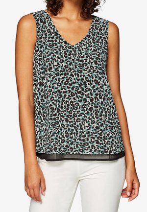 Haut sans manches à col en V avec imprimé léopard noir, turquoise et blanc, porté avec un pantalon blanc.