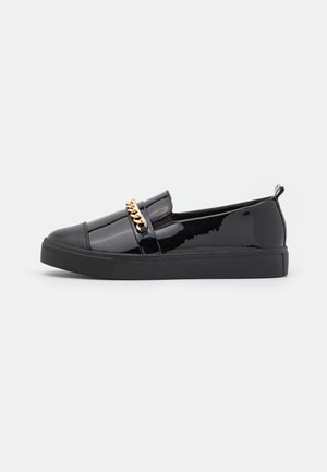 Chaussure à enfiler en cuir verni noir avec accent en chaîne dorée, bout rond, semelle en caoutchouc noir texturé et surface supérieure lisse.