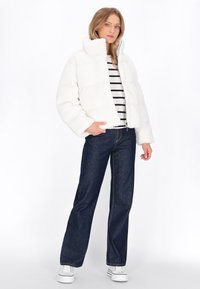 Witte, fluffy cropped jas met een hoge kraag, gedragen over een gestreept shirt. Gecombineerd met donkere denim, rechte broek en witte sneakers.