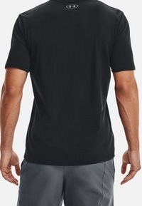 Svart kortärmad träningströja med en slät yta, försedda med en liten logotyp på övre delen av ryggen och en avslappnad passform. Bärs med grå shorts.