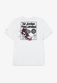 Balta medvilnė marškinėliai su atspausdintu rašiniu, vaizduojančiu raudonus ir juodus sportbačius, su tekstu "Air Jordan Has Landed" ir "100% odos" detalėmis.