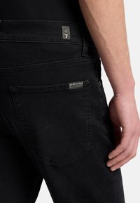 Schwarze Jeans aus Denim mit einer aufgenähten Tasche auf der Rückseite, kontrastierenden Nähten, Metallbeschlägen und einem strukturierten Markenlabel am Bund.