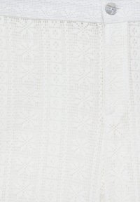 Tejido blanco con un patrón y una superficie texturizada, con un cierre de botón en la cintura y un diseño geométrico en toda su extensión.