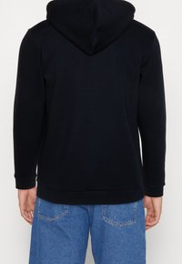 Černá mikina s kapucí vyrobená z měkké tkaniny, s klokaní kapsou a elastickými manžetami. Jednoduchý design bez vzorů nebo akcentů.