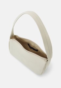Borsa in tessuto beige con manico curvo, chiusura con zip e un solo scomparto. Gli interni presentano un'etichetta. Texture liscia in tutto.