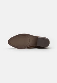 Suela de zapato de ante marrón, con un acabado suave y un patrón de agarre texturizado. Tacón cuadrado y punta redondeada para estabilidad y comodidad.