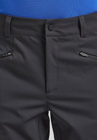 Pantaloni neri con una texture liscia e opaca, dotati di due tasche con zip e chiusura a bottone in vita.