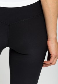 Leggings sportivi neri, tessuto liscio, vita alta, cuciture piatte, design aderente, senza motivi visibili, lunghi fino alla caviglia, minimal hardware.