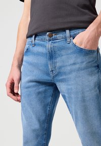 Vaqueros de denim azul claro con un corte clásico, que presentan un cierre de botón, cinco bolsillos y un sutil detalle texturizado en la tela.