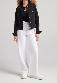 Black denim jacket with button closures, two chest pockets, and a fitted design. Paired with white high-waisted wide-leg jeans and white sneakers.