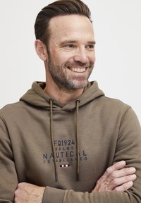 Hnedá mikina s kapucňou a námorníckym textom "FQ1924 BRAND NAUTICAL ESTABLISHED." Obsahuje šnúrky na kapucni a kontrastný akcent pod textom.