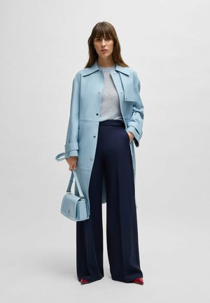Cappotto azzurro chiaro con chiusura a bottoni, maglione grigio, pantaloni larghi blu navy e una piccola borsa blu. Le scarpe rosse aggiungono un tocco di colore.