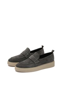 Mocasines de ante gris con punta redondeada, gruesa suela de goma beige y una correa decorativa en la parte frontal. Diseño minimalista con una textura suave.