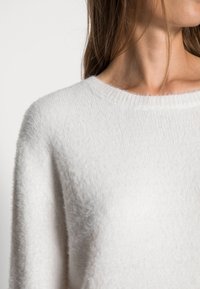 Valge, karvane sviiter ümmarguse kaelusega ja soonikkoes kaelusega. Omab pehmet tekstuuri ja veidi lahedat lõiget, rõhutades selle mugavat välimust.