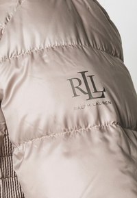 Ljusrosa puffjacka med kviltad textur. Har en framträdande svart logotyp "RLL RALPH LAUREN" tryckt på den övre ärmen.