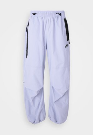 Svetlé lilacové nohavice Nike so elasticitou v páse, bočnými zipsovými vreckami a čiernymi akcentami. Tkanina má hladkú textúru a voľný strih.
