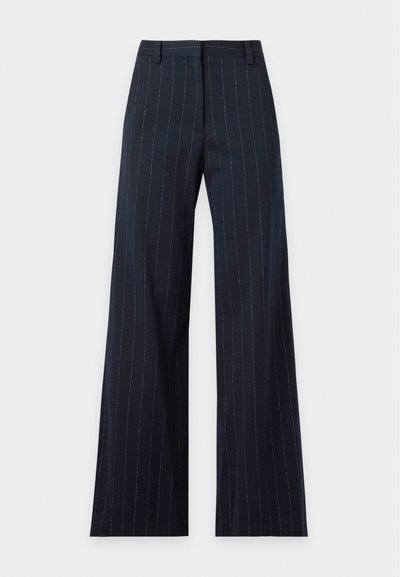 Pantalon large bleu marine avec fines rayures blanches verticales, passants de ceinture et fermeture éclair à l’avant.