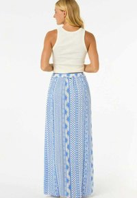 Larga falda maxi azul con un patrón geométrico blanco, hecha de una tela ligera con cintura elástica, combinada con una camiseta sin mangas ajustada blanca.