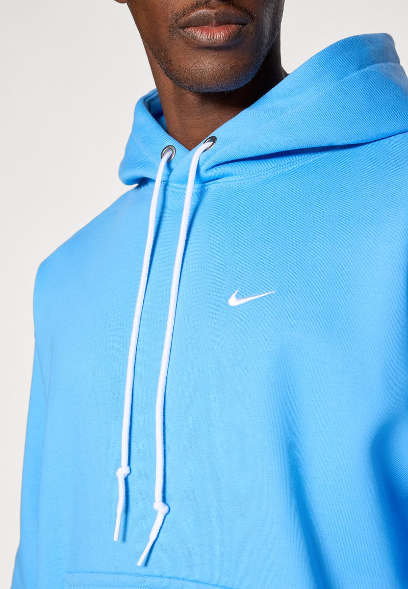 Blauer Baumwollhoodie mit Kordelzug, ausgestattet mit einem kleinen weißen Nike-Logo. Glatte Textur, reguläre Passform und verstellbare Kapuze.