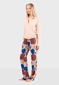 Chemise polo rose clair à manches longues avec col, assortie à un pantalon de pyjama floral bleu, rouge et marron sur fond beige. Tissu doux.