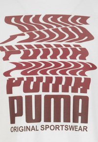 T-shirt bianco con testo grafico rosso in grassetto, che presenta il logo "PUMA" sovrapposto e "ORIGINAL SPORTSWEAR" in un grande carattere, con motivi vari.