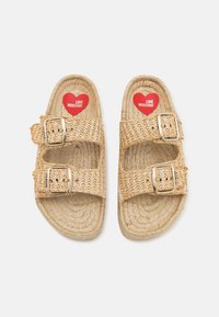 Beige austs ar izstrādāti no austa salmiem ar divām regulējamām zelta tonētiem sprādzēm. Tie ir aprīkoti ar mīkstu zoli, kurā iekšpusē ir sarkans sirds logotips.