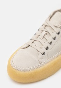 Sneaker in suede beige con suola in gomma crema, punta rotonda e occhielli neri. Presenta cuciture a contrasto lungo la suola. Design classico con lacci.