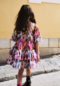 Farverig lagdelte kjole med korte pufærmer, prydet med et blomsterprint i pink, blå og brun. Bæres med sorte støvler og pink sokker.