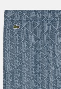 Blauwe stoffen met een patroon van geometrische vormen en een gestructureerd oppervlak. Inclusief een klein groen Lacoste-logo op de tailleband.