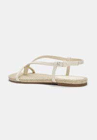 Vita espadriller med vävda tygremmar och en platt jutesula. Designen inkluderar ett smalt ankelband med ett silverfärgat spänne.