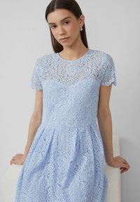 Hellblaues Spitzenkleid mit kurzen Ärmeln, floralem Muster, gewellten Kanten und einem taillierten Oberteil mit einem ausgestellten Rock.