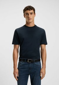 Navy blue short-sleeve T-shirt in textured fabric with a round neck; paired with dark blue jeans and a black belt.