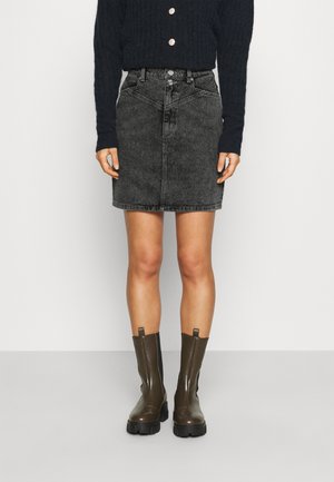 Person wearing a black textured sweater, gray denim mini skirt, and dark brown chunky Chelsea boots, standing against a plain background.
