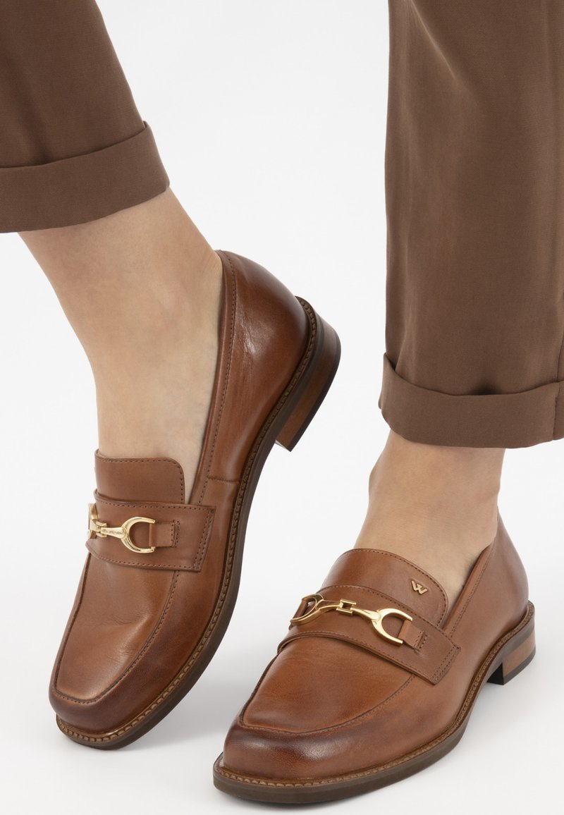 Mocassins en cuir brun avec accent en mors de cheval doré, texture lisse, design à bout carré et petit talon empilé. Pantalons retroussés au niveau de l'ourlet.