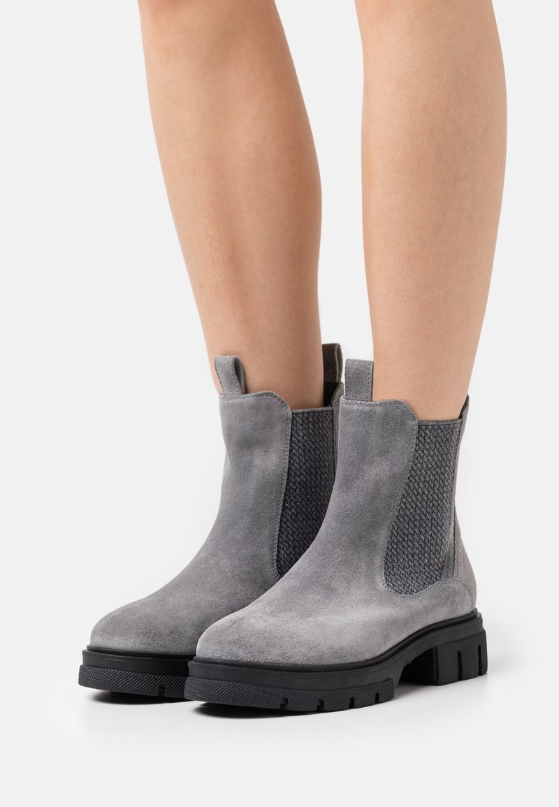 Bottes basses en daim gris avec panneaux latéraux élastiques texturés et languettes de tirage. Semelle épaisse en caoutchouc noir avec rainures antidérapantes.