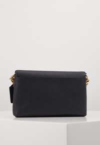 Pochette en cuir noir avec une finition texturée, dotée d'une chaîne en or et d'un fermoir. Forme rectangulaire avec un design minimaliste.