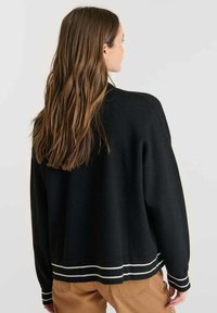 Maglione nero a collo giro con righe bianche sull'orlo, caratterizzato da una vestibilità comoda e una texture a coste, visto da dietro.