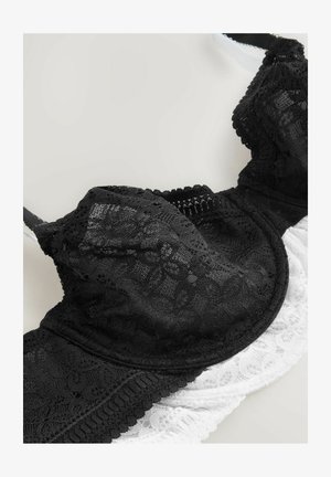 Black and white lace bra featuring floral pattern, padded cups, adjustable straps, and scalloped edges. Soft texture with detailed stitching.