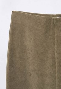 Tissu côtelé de couleur vert olive avec une texture lisse. L'article présente une taille haute et une coupe épurée et moderne, mettant en valeur sa forme élancée.