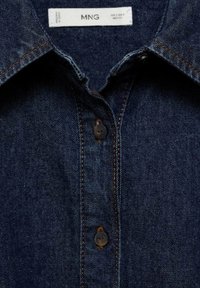 Chemise en denim noir avec un col classique, des boutons noirs et des coutures orange contrastantes le long des coutures. L'étiquette indique "MNG."