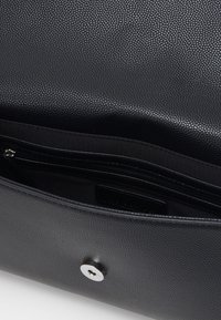 Black textured leather bag with a smooth interior, featuring a zip pocket and a magnetic closure detail.