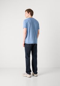 T-shirt de algodão azul com decote redondo e mangas curtas, combinada com jeans de algodão escuro. O conjunto tem um corte casual e um design básico.