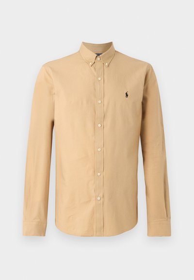 Langermet skjorte i lys beige bomull. Har spiss krage og en liten svart logo på venstre bryst. Glatt tekstur.