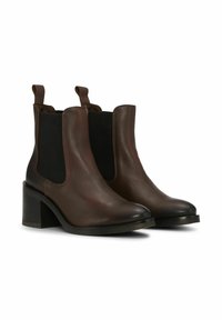 Smeđe kožne gležnjače s elastičnim bočnim panelima, blago šiljastim vrhovima i masivnom crnom petom. Glatke teksture i minimalnih detalja.